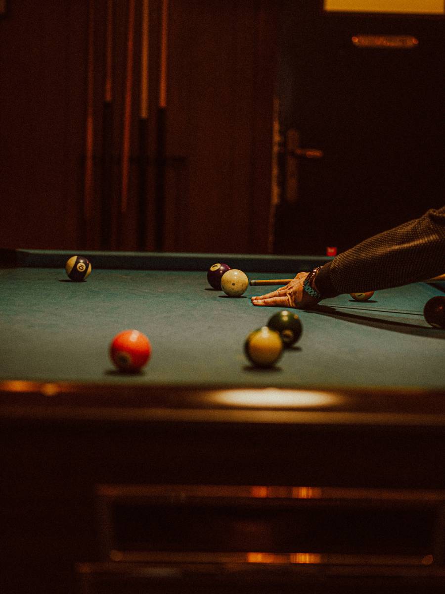 Table de billard éclairée dans la pénombre, un joueur prêt à casser.