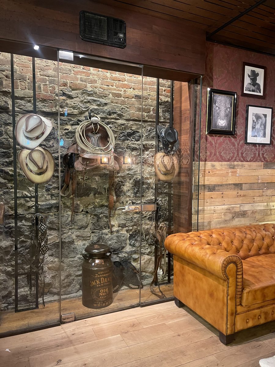 Vitrine western : selle, chapeaux de cowboy et bottes devant un mur de pierre.